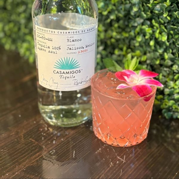 Casamigos Blanco tequila bottle next to a pink cocktail garnished with a fuchsia orchid.