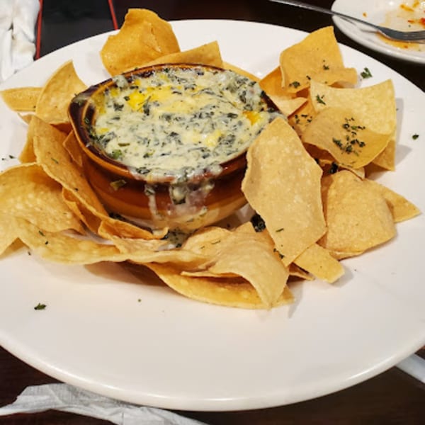 A bowl of creamy spinach dip with melted cheese, surrounded by golden tortilla chips on a white plate.