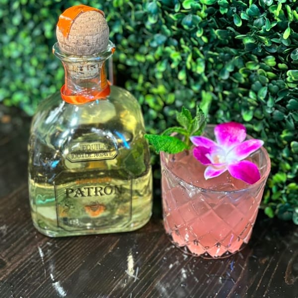 Patron tequila bottle next to a pink cocktail garnished with mint and an orchid.