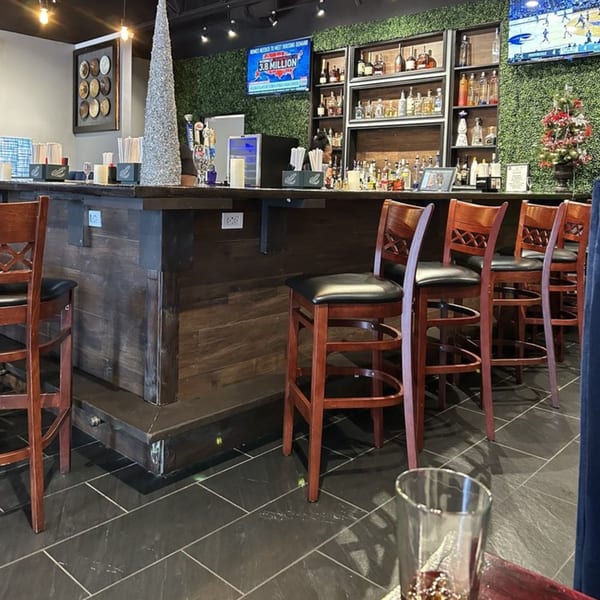A dark wood bar with several stools, liquor bottles, and TVs, against a green wall.
