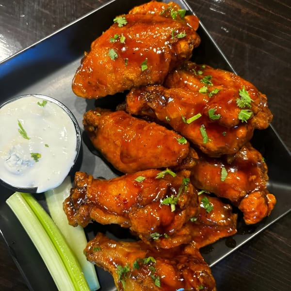 Snooks Grill & Cocktails' buffalo wings with blue cheese dressing and celery sticks on a black plate.