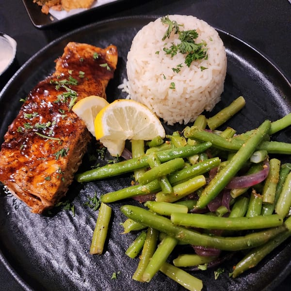 Snooks Grill & Cocktails' salmon with glaze, rice, green beans, and lemon slices on a black plate.