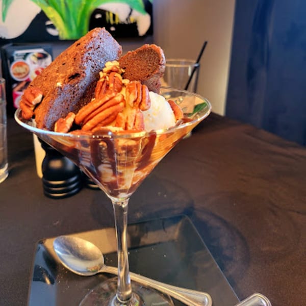 Brownie sundae with vanilla ice cream, chocolate syrup, and pecans in a martini glass.