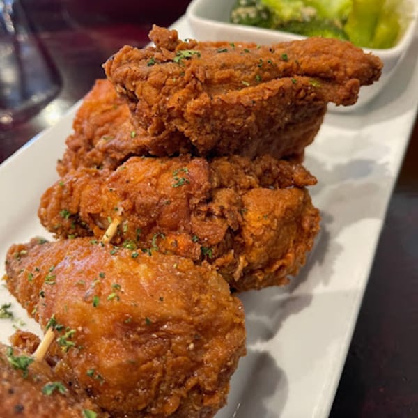 Crispy fried chicken pieces, garnished with herbs, on a white rectangular plate with a side of greens.