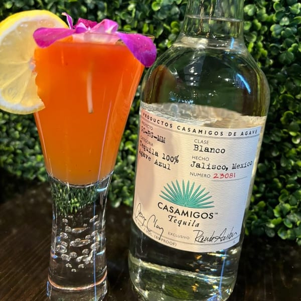 A vibrant orange cocktail with a lemon slice and purple flower next to a bottle of Casamigos Tequila.