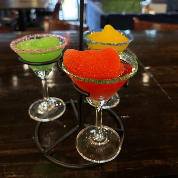 Three colorful frozen margaritas, red, green, and yellow, in martini glasses on a dark wooden table.