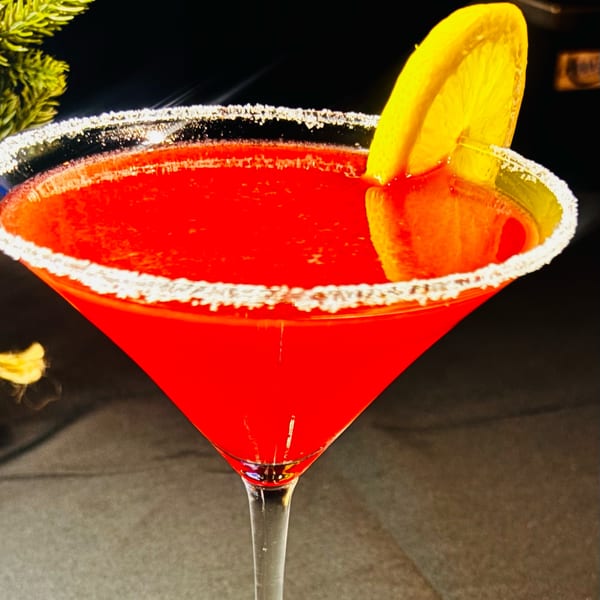 A vibrant red cocktail in a sugar-rimmed martini glass, garnished with a lemon slice.